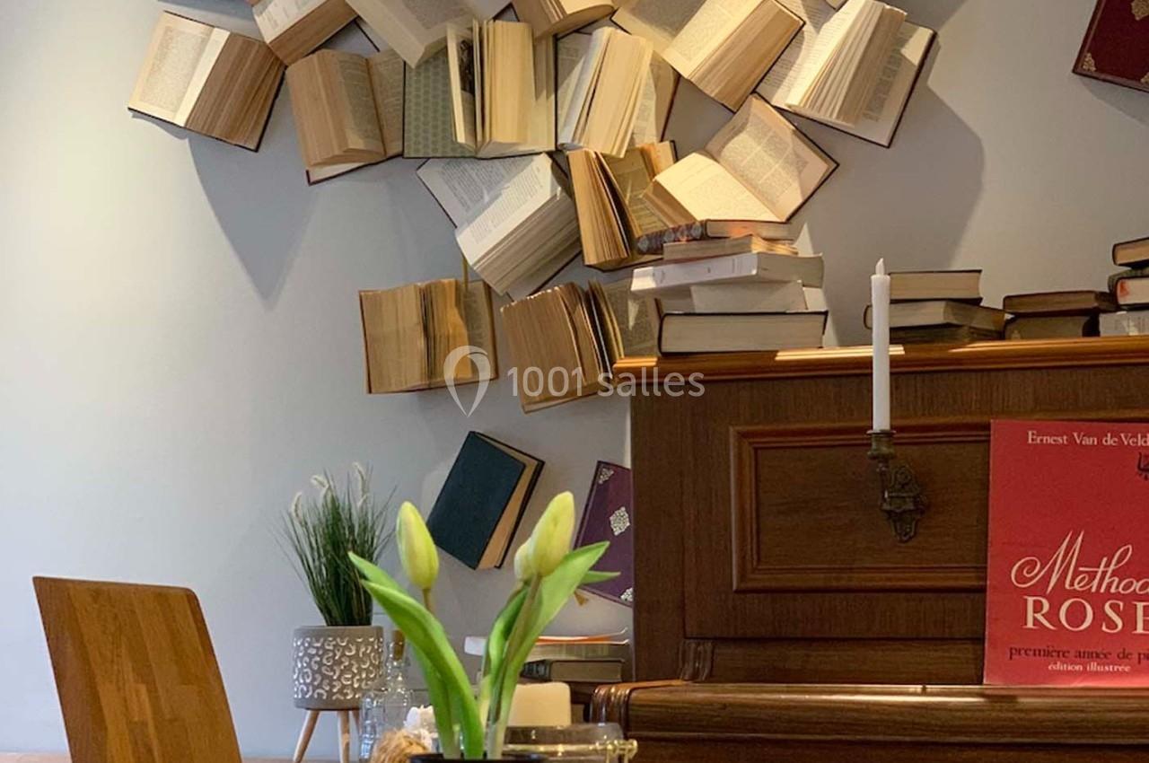 Des livres ouverts fixés au mur au-dessus d'un piano, avec une bougie et un vase de fleurs au premier plan.