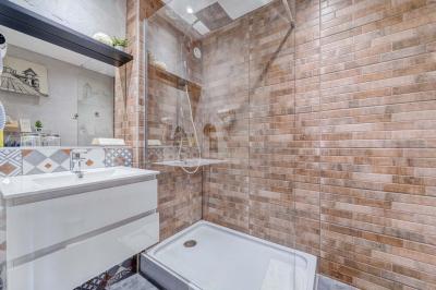 Salle de bain avec douche à l'italienne, carrelage effet brique, vasque blanche et miroir au mur.