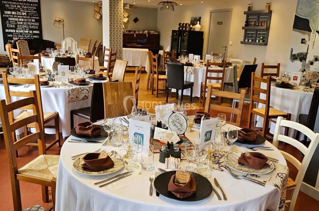 Salle de restaurant décorée avec des tables rondes dressées, nappes blanches, serviettes marron et vaisselle élégante.