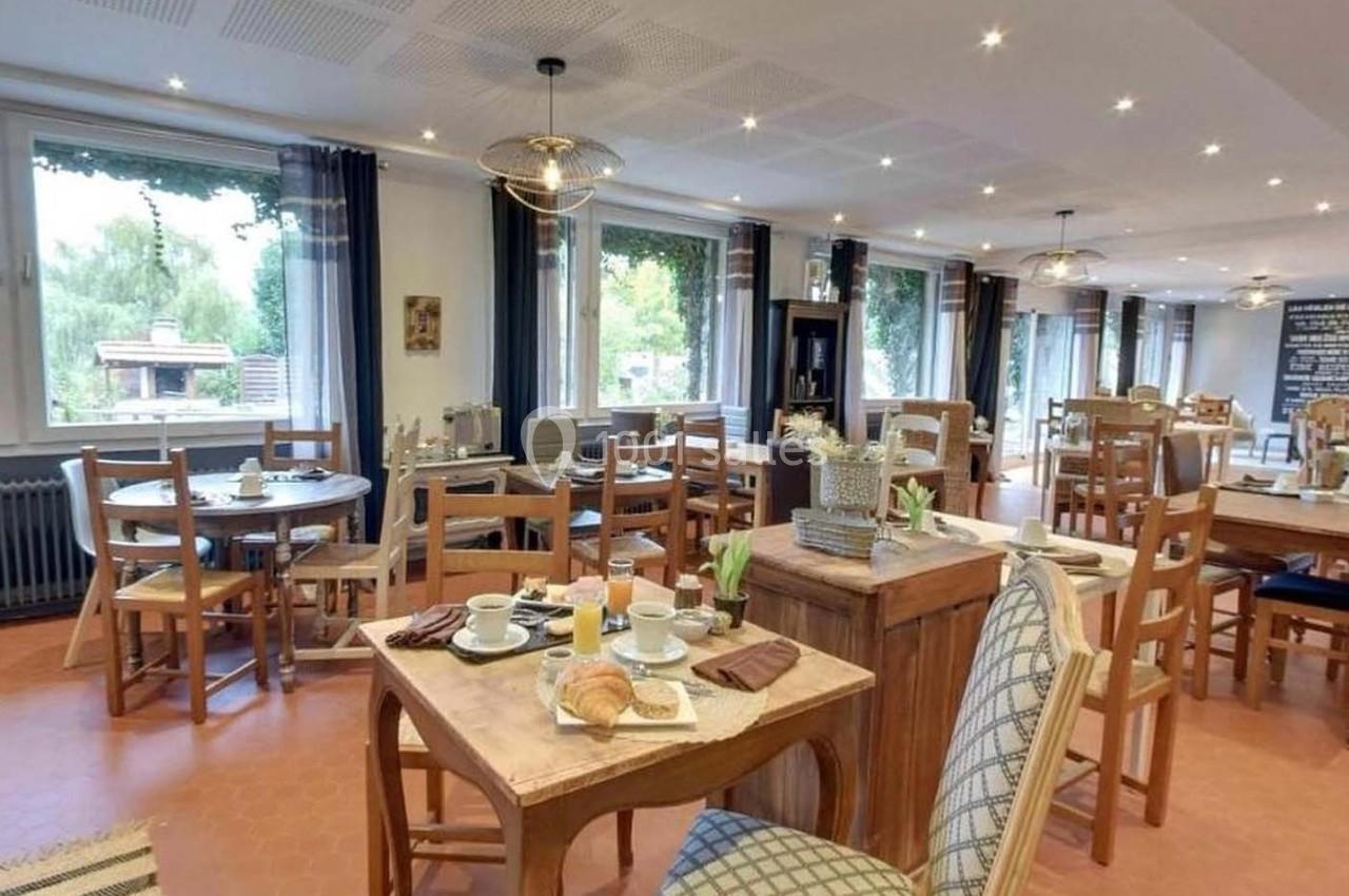 Salle de restaurant lumineuse avec tables en bois dressées pour le petit-déjeuner, vue sur l'extérieur verdoyant.