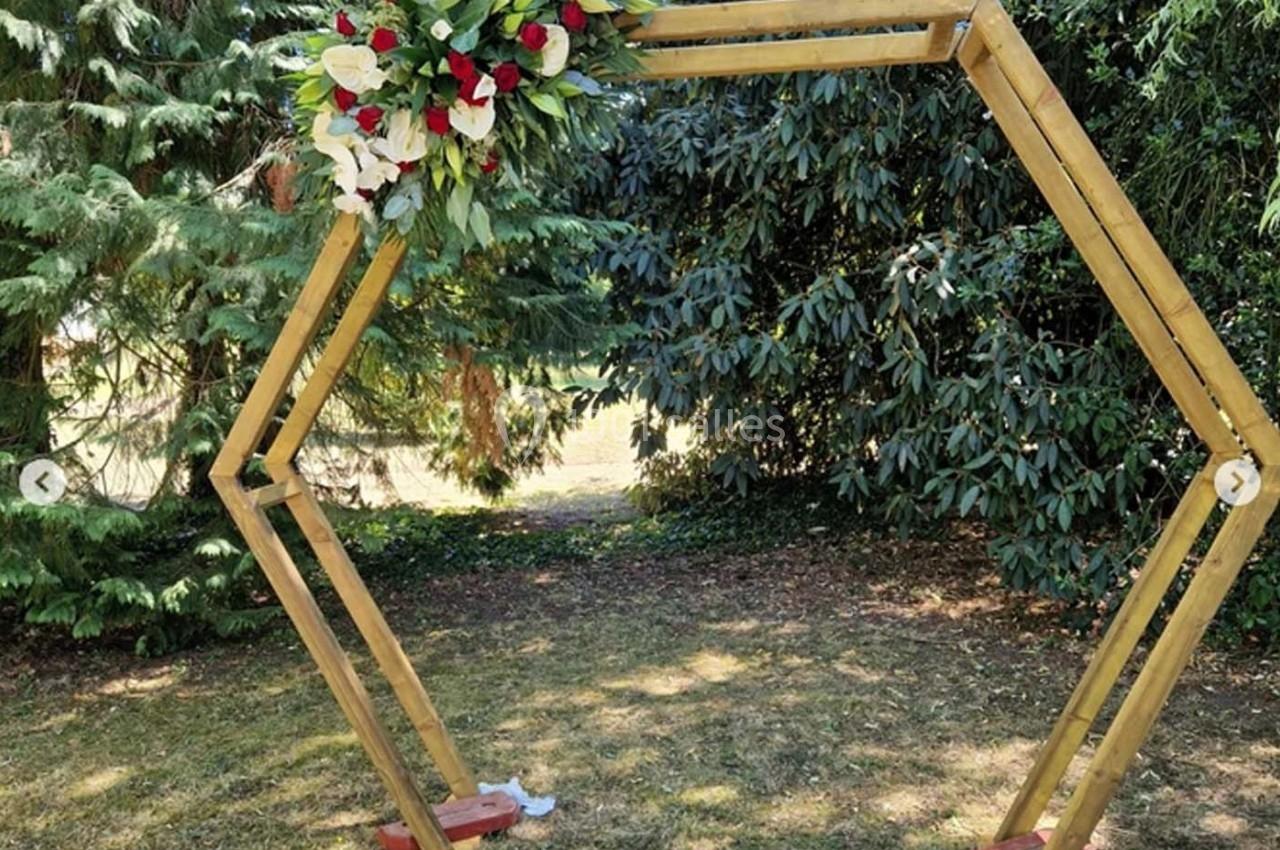Structure hexagonale en bois décorée de fleurs rouges et blanches, installée dans un jardin verdoyant.