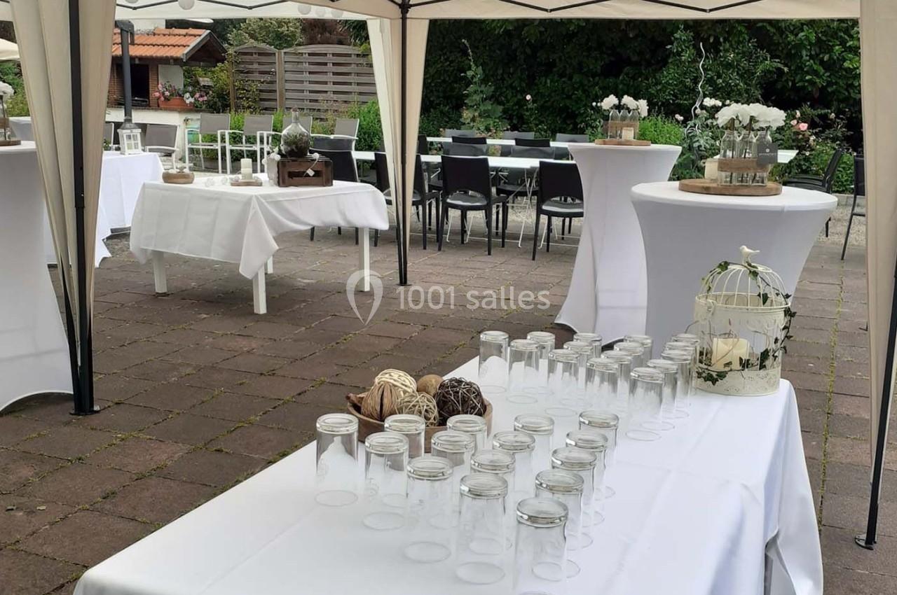 Tables décorées pour un événement en extérieur, avec nappes blanches, pots en verre et éléments décoratifs.
