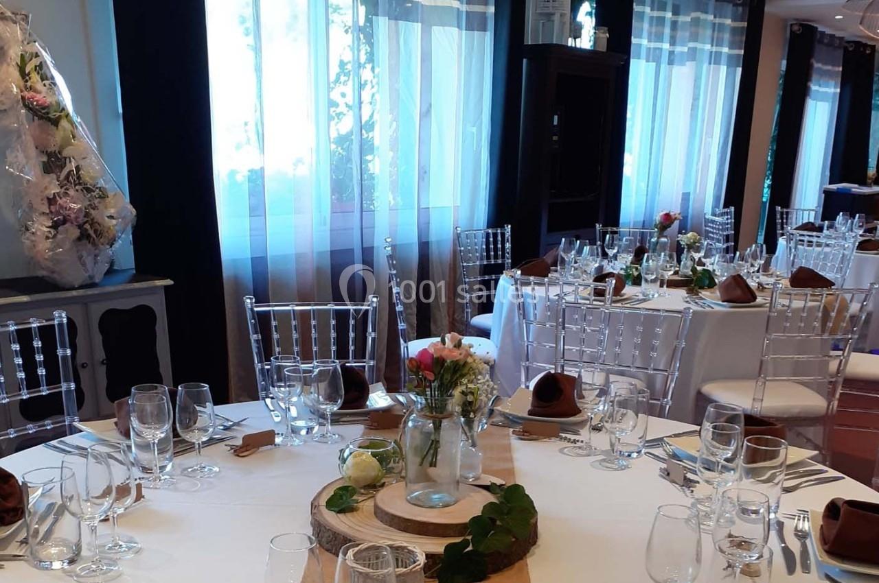 Salle de réception décorée avec des tables rondes dressées, nappes blanches et centres de table floraux.
