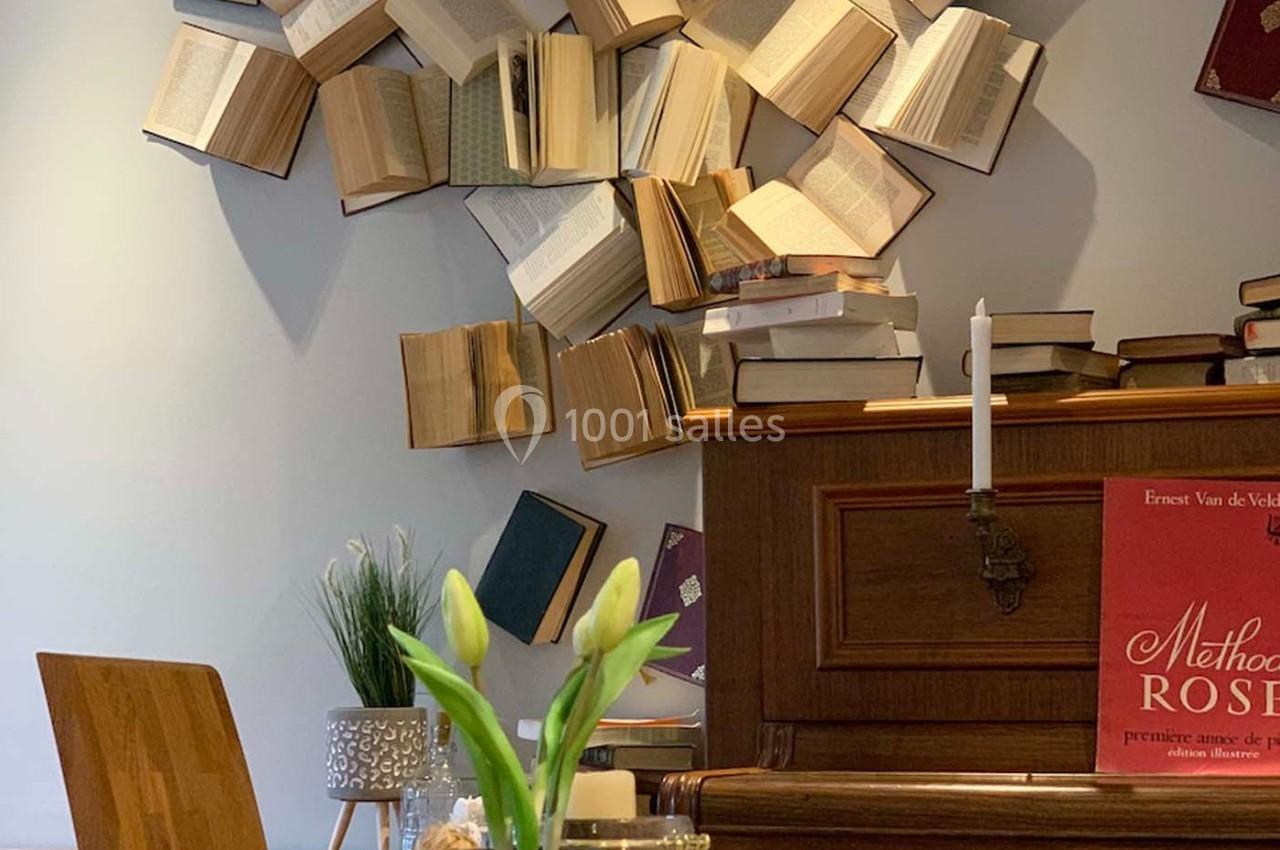 Des livres ouverts fixés au mur au-dessus d'un piano en bois, avec des fleurs et une bougie en premier plan.