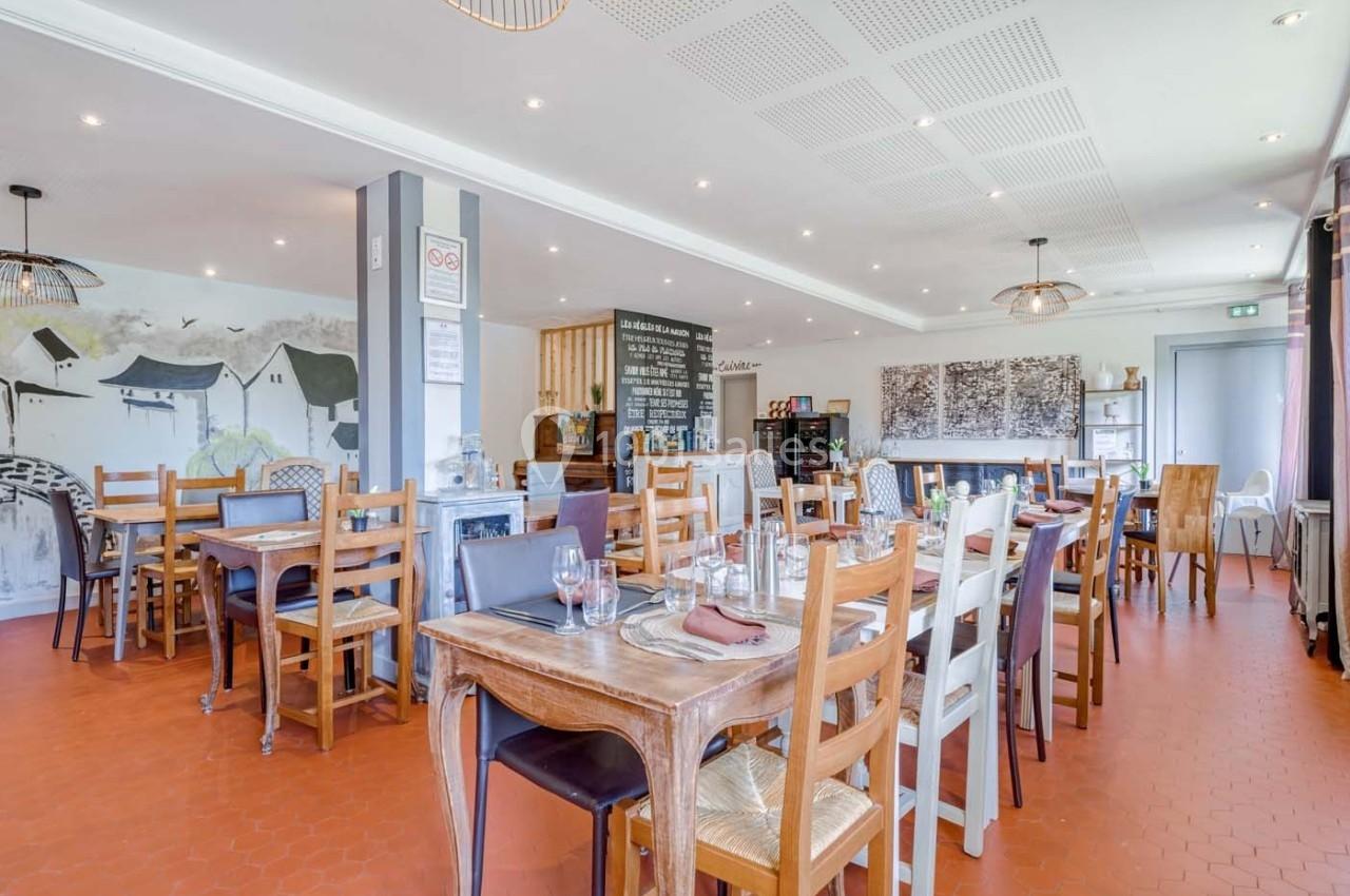 Salle de restaurant lumineuse avec tables en bois, chaises variées et décoration murale sobre.