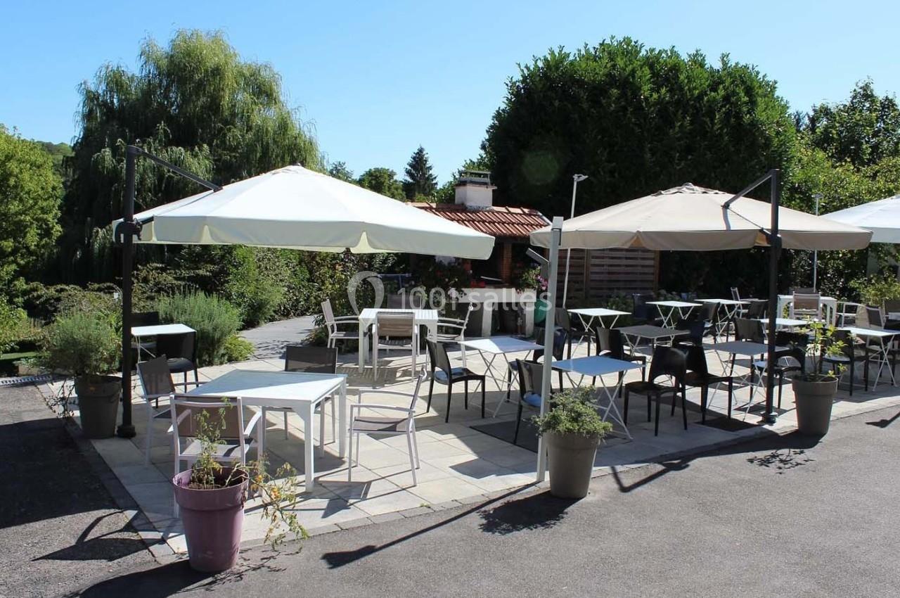 Terrasse extérieure avec tables et chaises sous des parasols, entourée de végétation et baignée de lumière naturelle.