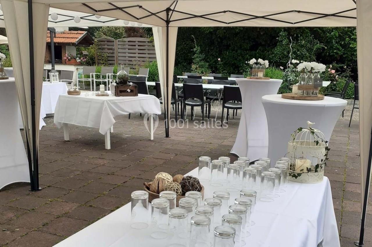 Tables décorées sous des tonnelles blanches dans un jardin, préparées pour un événement en extérieur.