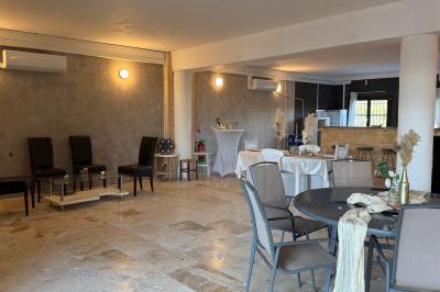 Salle lumineuse avec une grande table décorée de fleurs roses, entourée de chaises blanches, et un espace en arrière-plan.