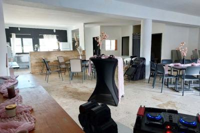 Salle lumineuse avec une grande table décorée de fleurs roses, entourée de chaises blanches, et un espace en arrière-plan.