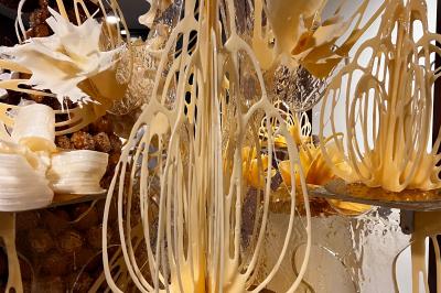 Miniature Scpa Visualproduction #12 Pièce montée en choux décorée de fleurs en sucre et de motifs en chocolat blanc, posée devant un mur de briques.