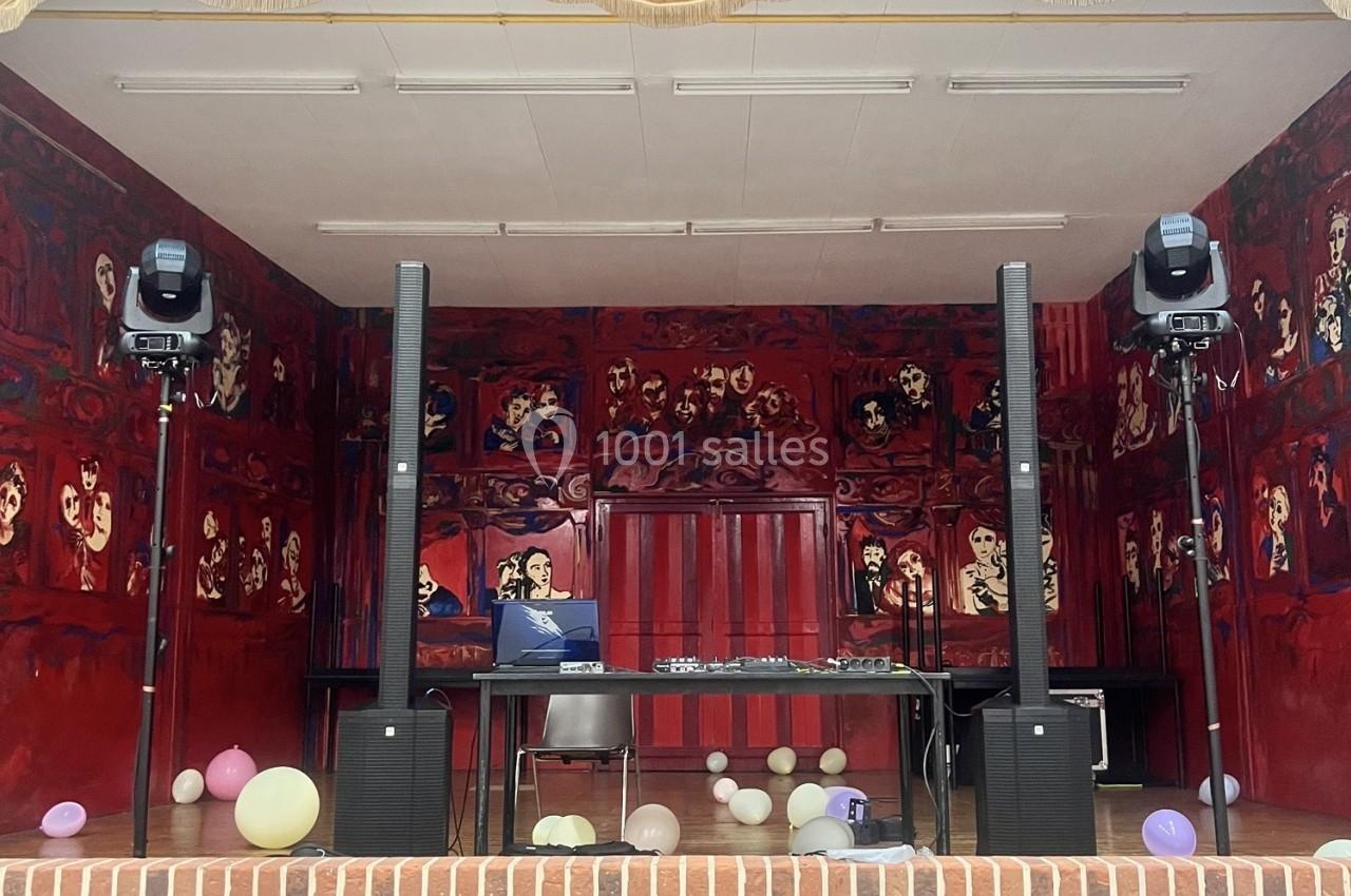 Scène décorée de peintures rouges avec une table de mixage, des enceintes et des ballons au sol.