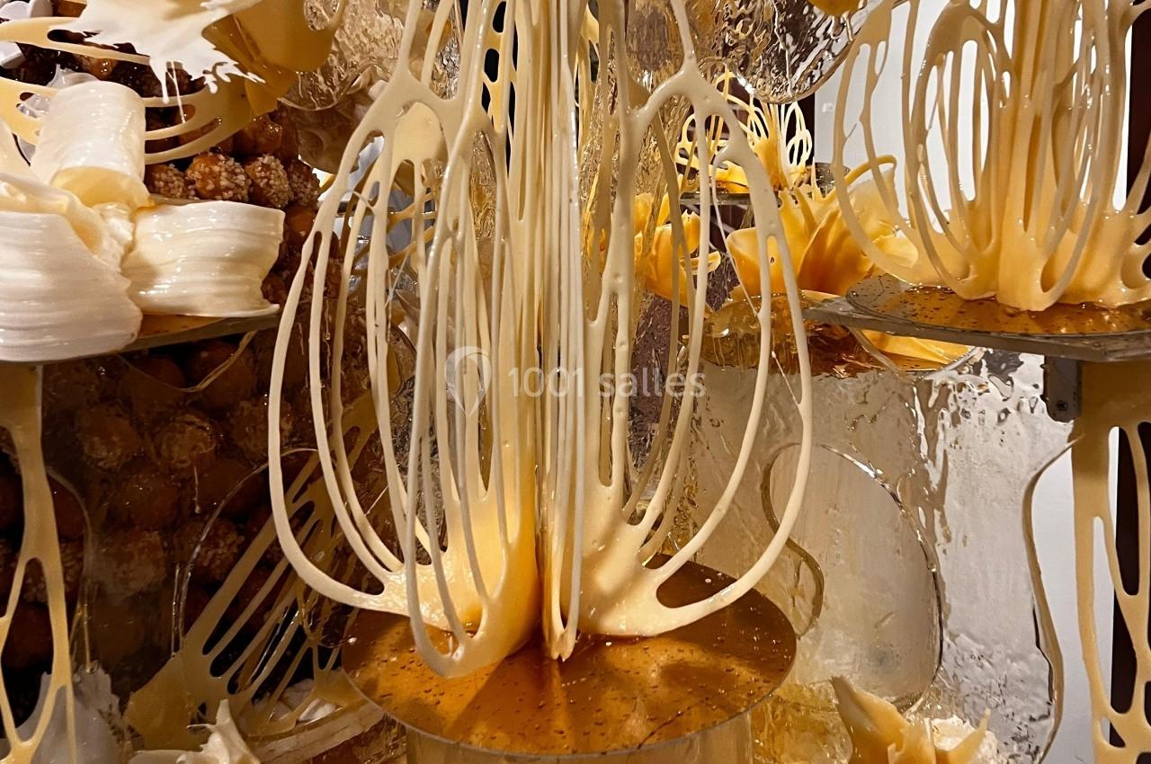 Fils de caramel fondant tombant sur des supports métalliques, entourés de textures sucrées et dorées.