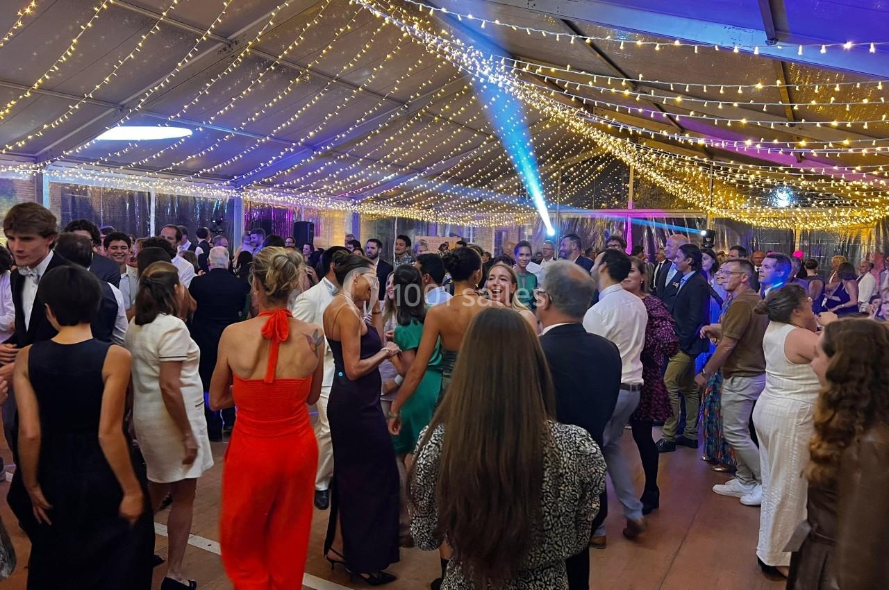 Des personnes dansent sous une tente décorée de guirlandes lumineuses lors d'une soirée festive.