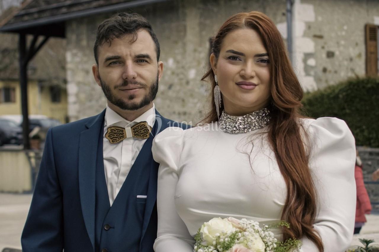 Un couple en tenue de mariage pose devant un bâtiment en pierre dans un cadre extérieur.