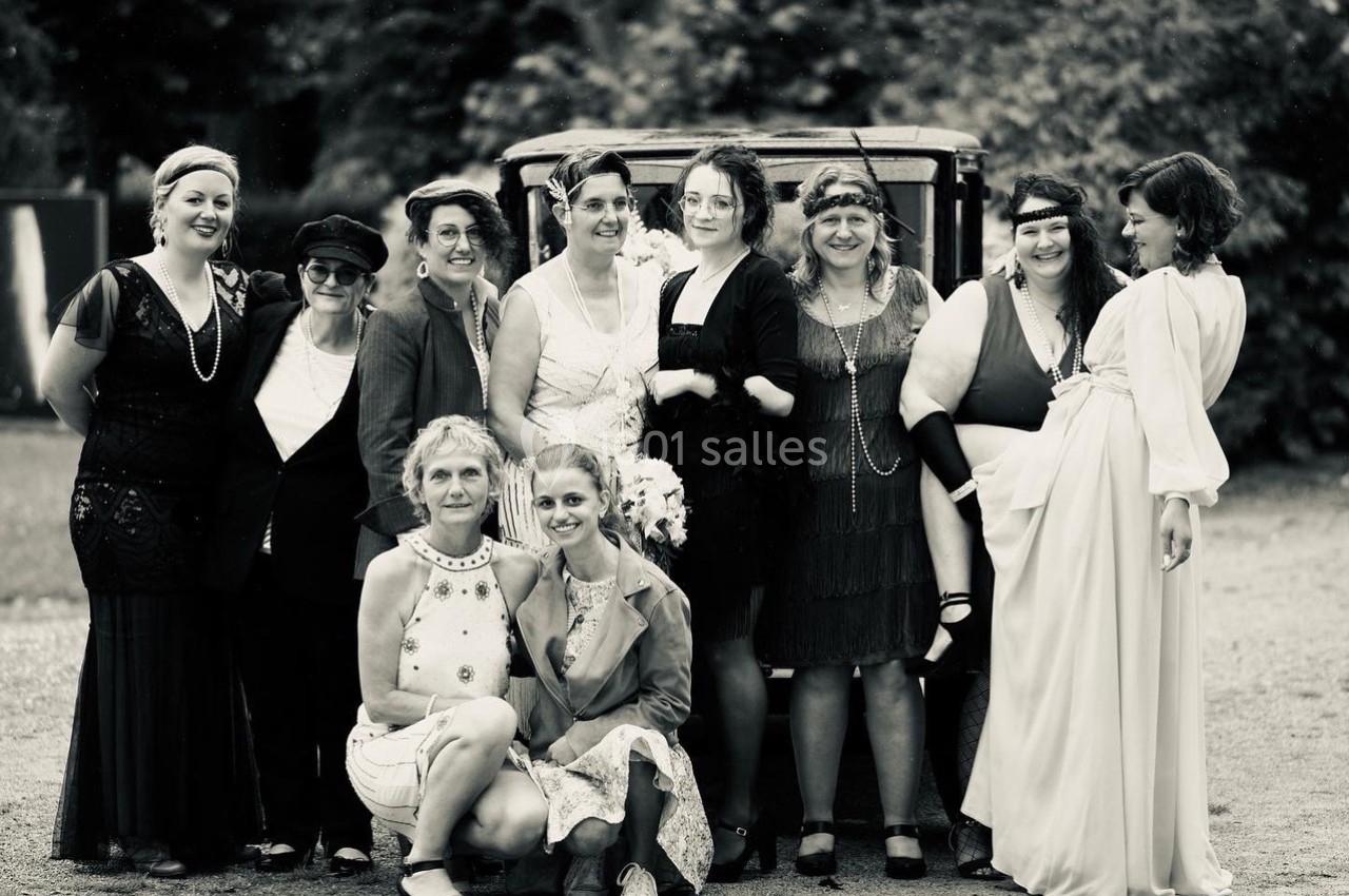 Un groupe de femmes en tenue vintage pose devant une voiture ancienne dans un cadre extérieur.