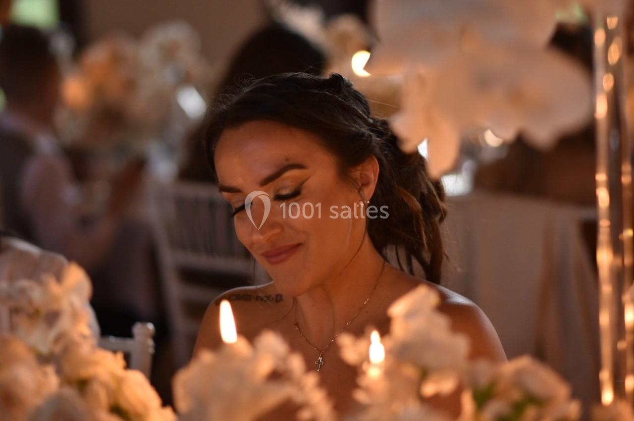 Femme souriante assise à une table décorée de fleurs blanches et illuminée par des bougies dans une ambiance tamisée.