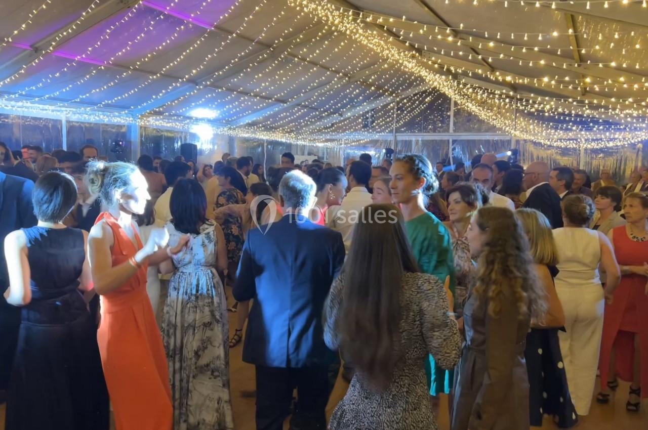 Personnes élégamment vêtues discutant et dansant sous une tente illuminée par des guirlandes lumineuses.