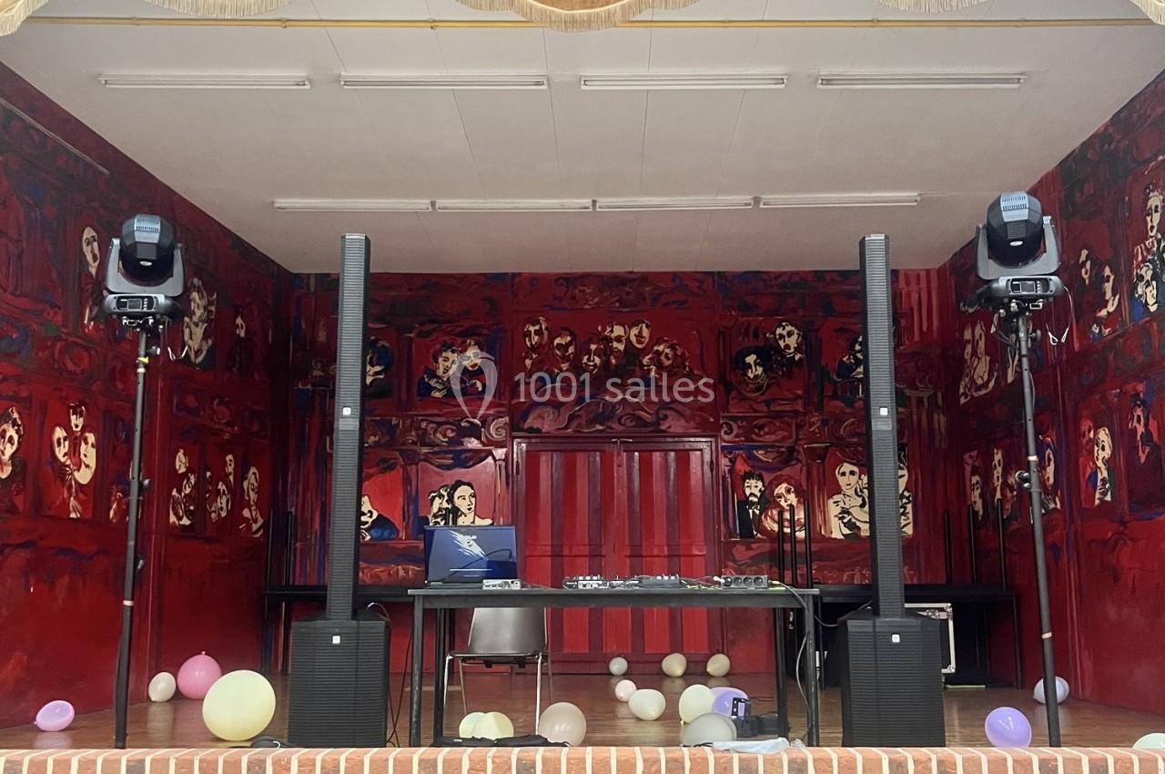 Scène décorée de peintures rouges avec des enceintes, une table, des chaises et des ballons au sol.