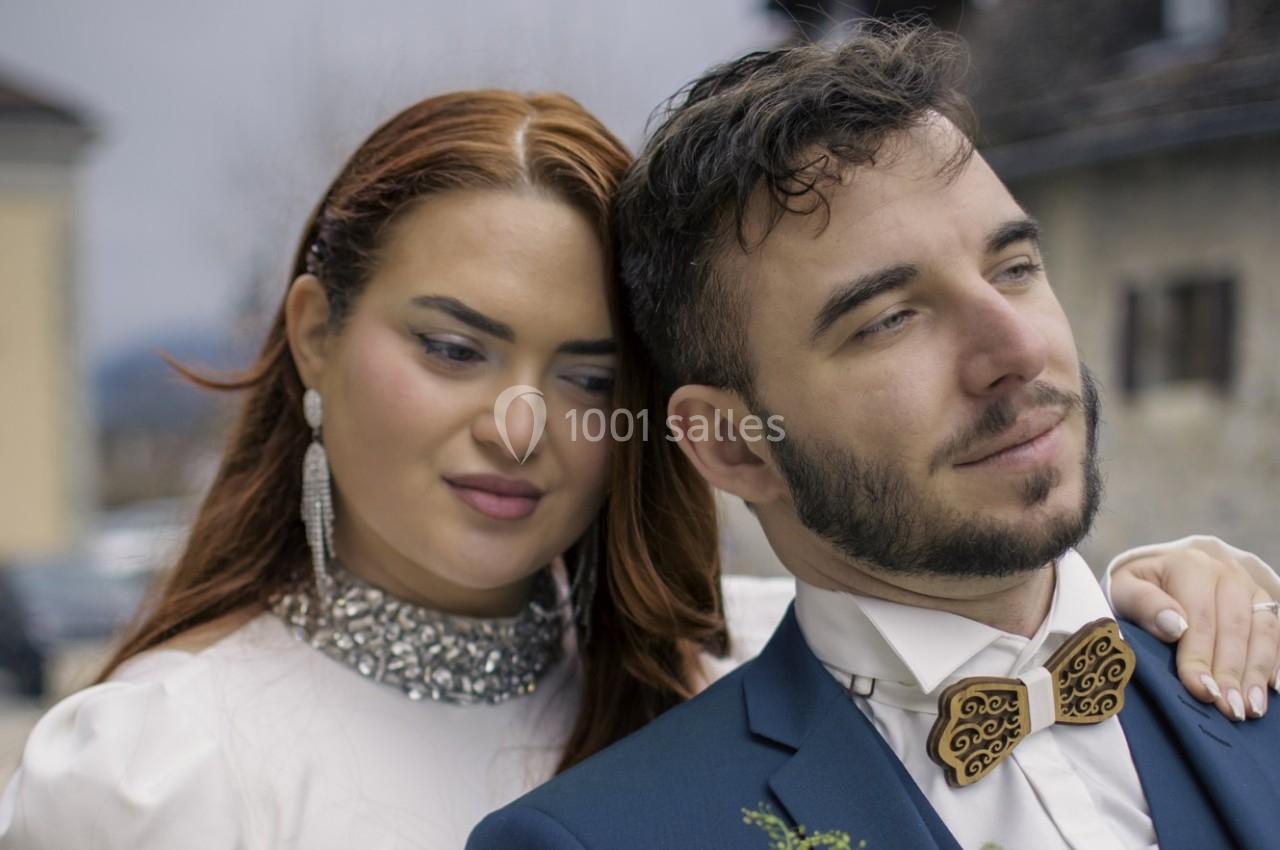 Un couple habillé élégamment, l'homme en costume et la femme en robe blanche, pose en extérieur.