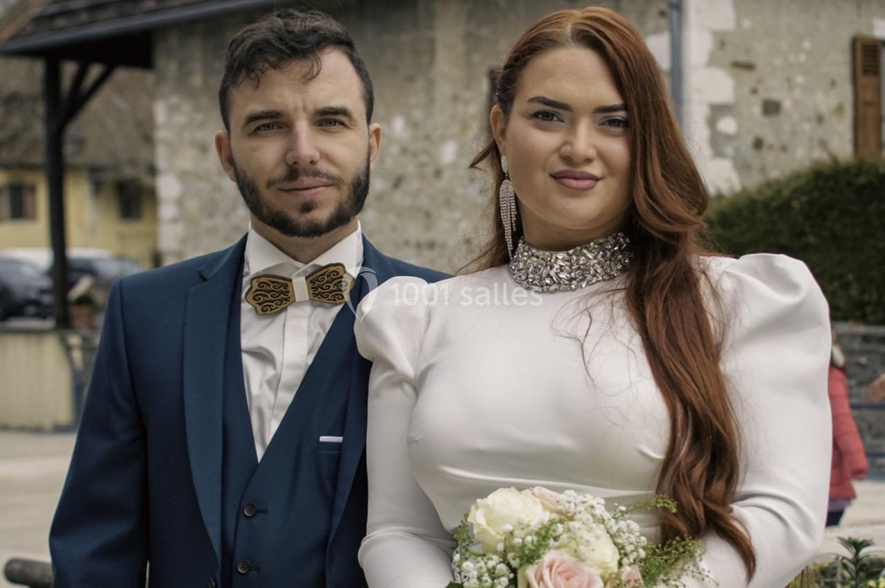 Un couple en tenue de mariage pose à l'extérieur, la mariée tenant un bouquet de fleurs.