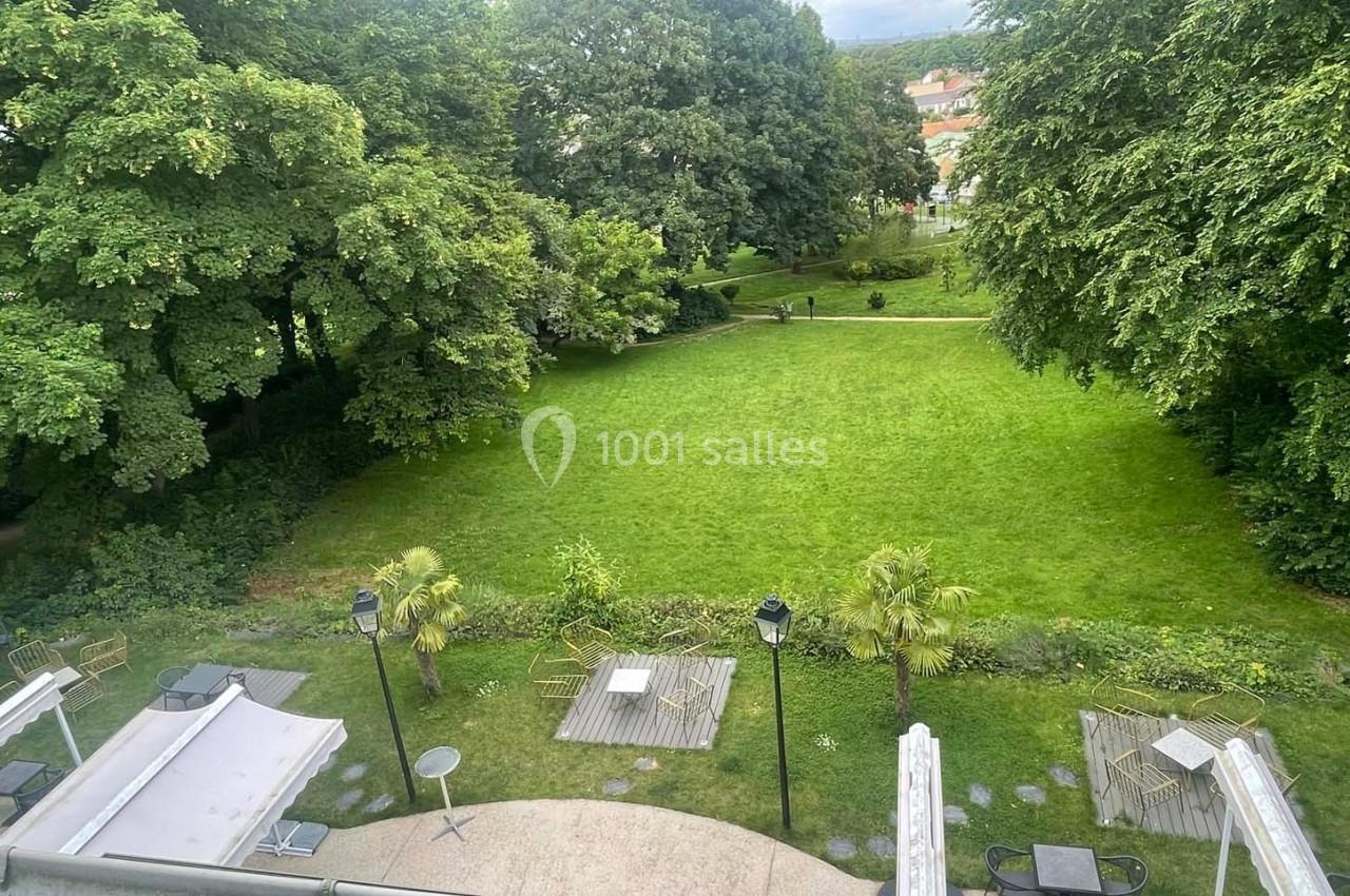 Vue d'un jardin verdoyant avec pelouse, arbres et terrasses aménagées, capturée depuis un point en hauteur.