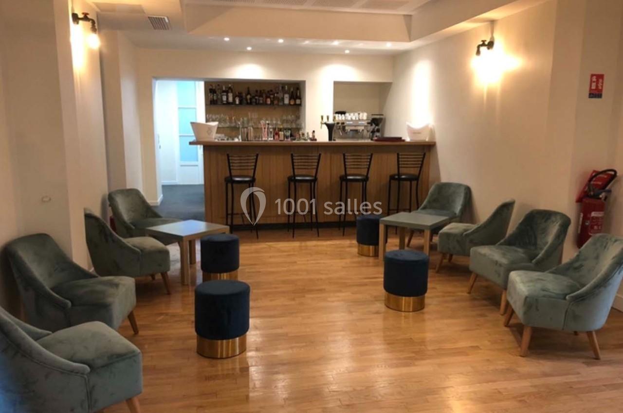 Salle avec un bar en bois, des fauteuils verts, des tabourets bleus et un sol en parquet clair.