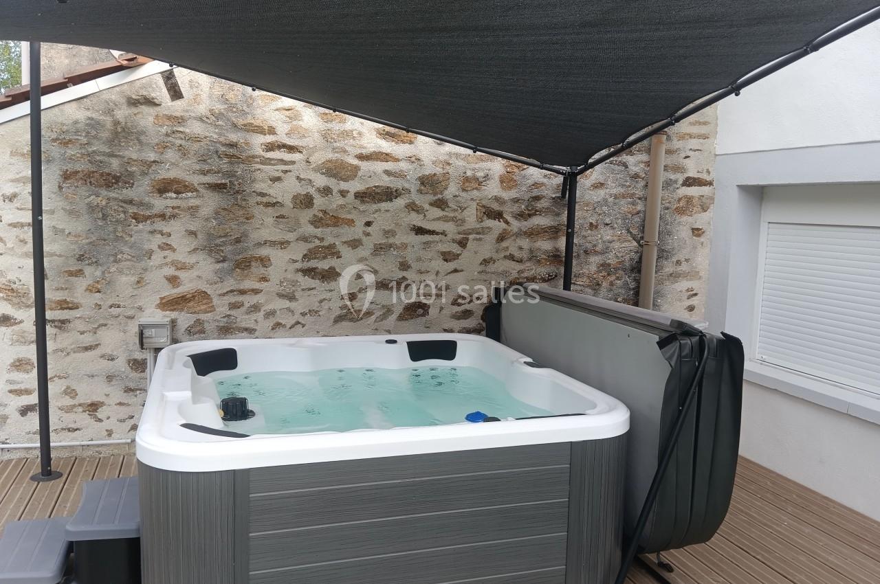 Jacuzzi extérieur rempli d'eau, installé sur une terrasse en bois, protégé par une toile d'ombrage.