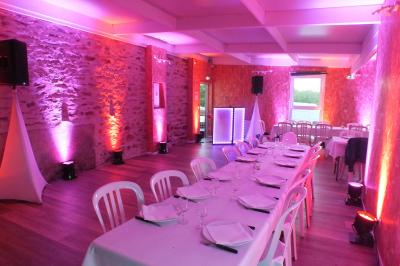 Cour extérieure avec sol en gazon synthétique, tables, chaises empilées et plantes en pots, entourée de bâtiments en bois.