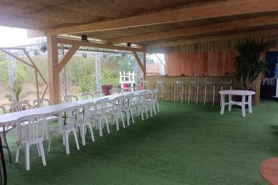 Cour extérieure avec sol en gazon synthétique, tables, chaises empilées et plantes en pots, entourée de bâtiments en bois.