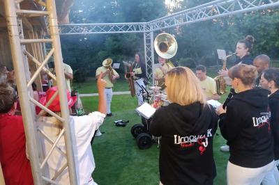 Cour extérieure avec sol en gazon synthétique, tables, chaises empilées et plantes en pots, entourée de bâtiments en bois.