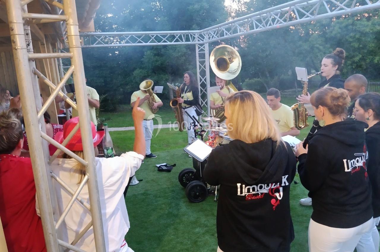 Un groupe de musiciens joue en plein air sous une structure métallique, entouré de spectateurs.