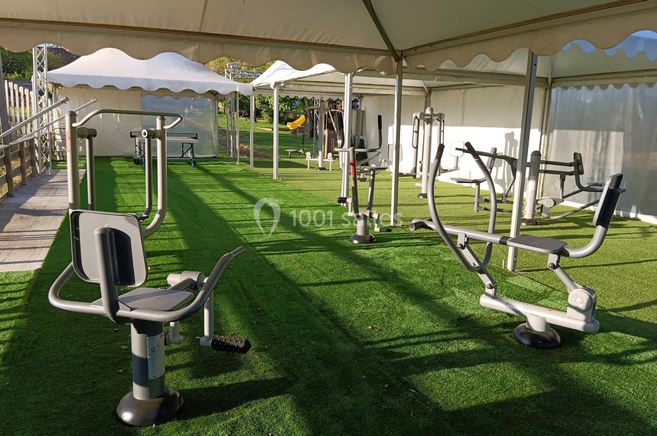 Équipements de fitness en plein air installés sous une tente sur une surface en gazon synthétique.