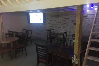 Cour extérieure avec sol en gazon synthétique, tables, chaises empilées et plantes en pots, entourée de bâtiments en bois.