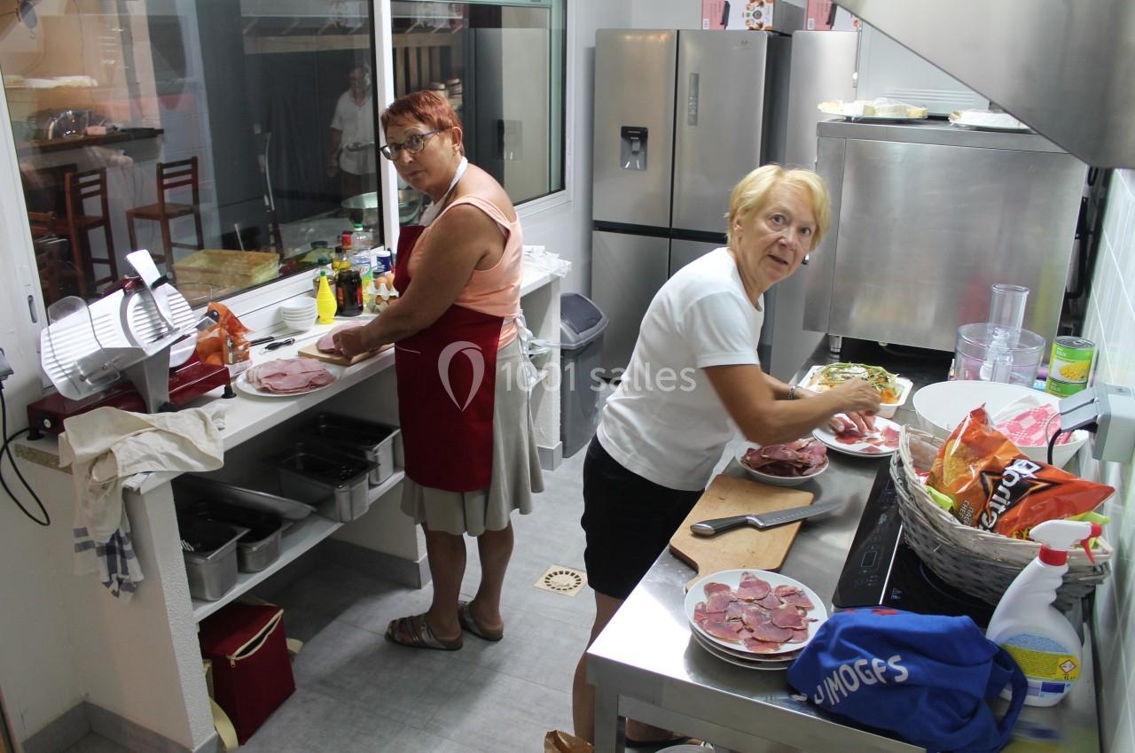 Deux femmes préparent des assiettes de charcuterie dans une cuisine professionnelle équipée.