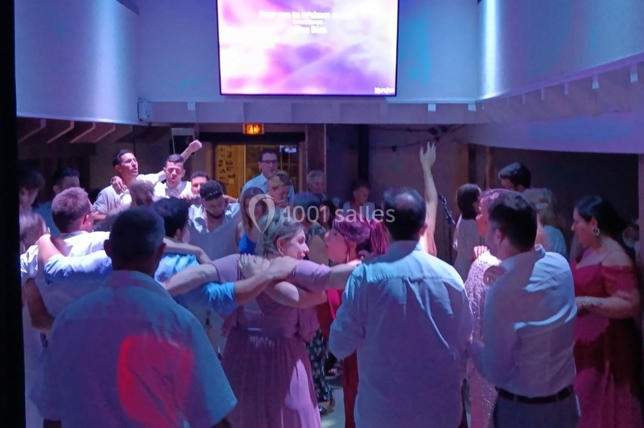 Groupe de personnes dansant dans une salle éclairée par des lumières colorées, avec un écran en arrière-plan.
