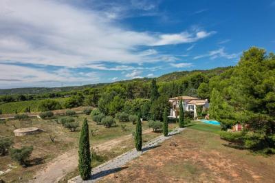 Salon avec canapé beige, fauteuils, table basse, télévision, cheminée en pierre et plafond avec poutres apparentes.