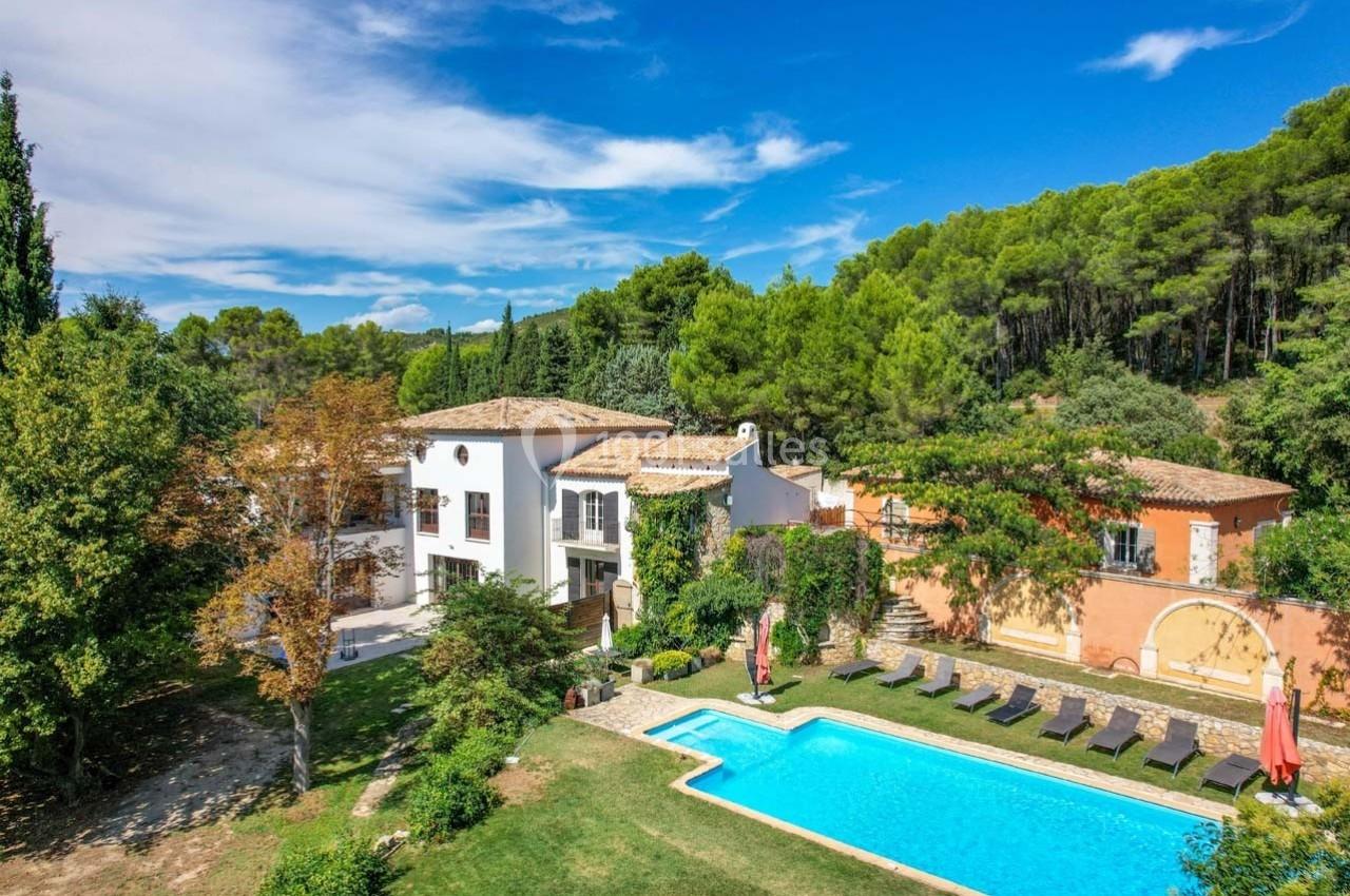 Vue aérienne d'une maison provençale entourée de végétation, avec piscine, transats et ciel dégagé.