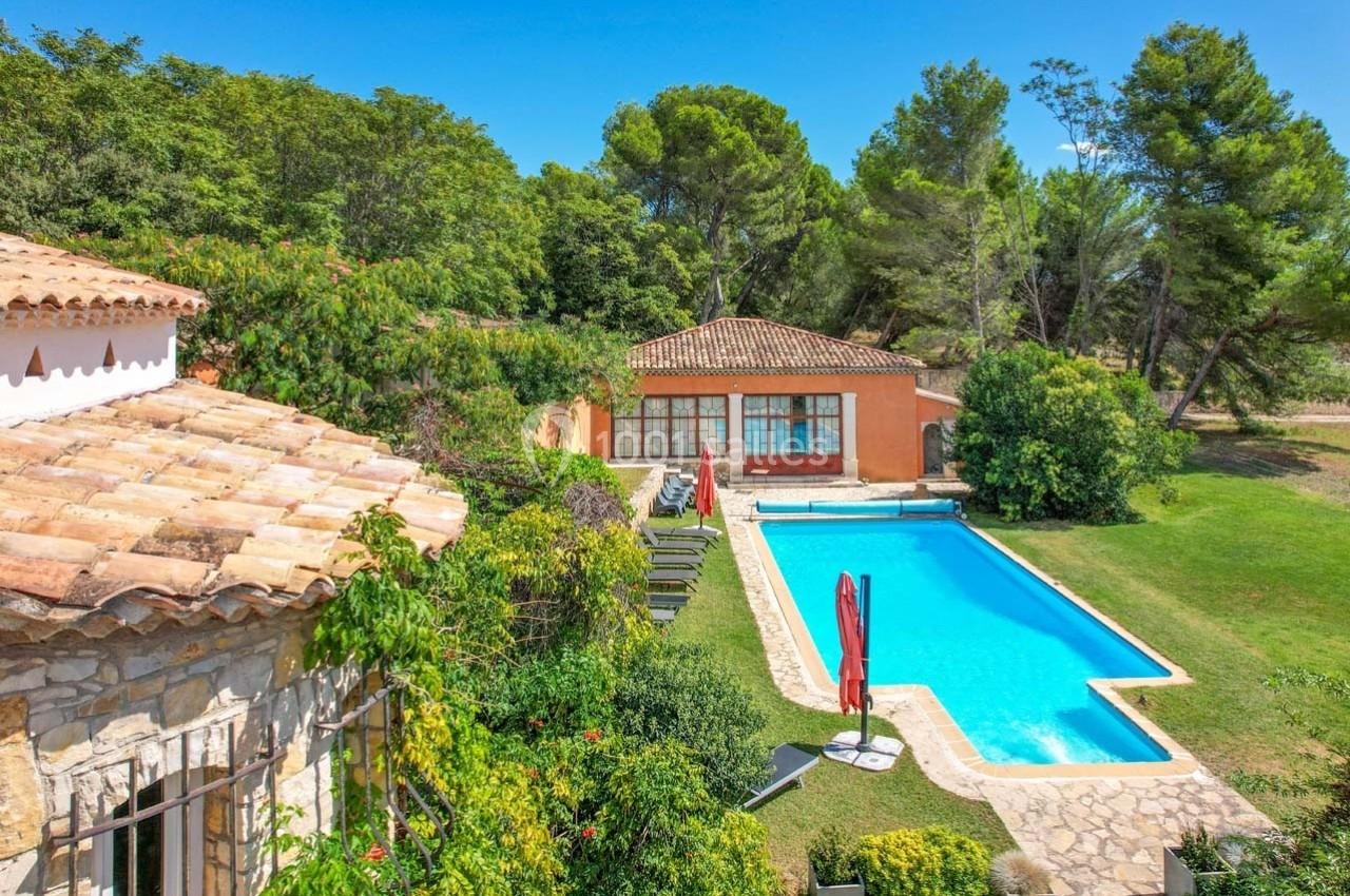 Maison avec piscine entourée de verdure, terrasse et chaises longues, située dans un cadre arboré et ensoleillé.