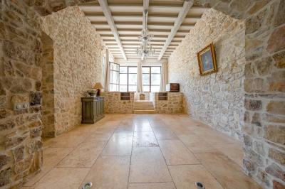 Salon avec canapé beige, fauteuils, table basse, télévision, cheminée en pierre et plafond avec poutres apparentes.