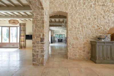Salon avec canapé beige, fauteuils, table basse, télévision, cheminée en pierre et plafond avec poutres apparentes.