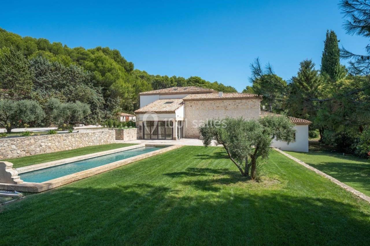 Maison en pierre entourée de verdure avec une piscine rectangulaire et un grand jardin arboré.