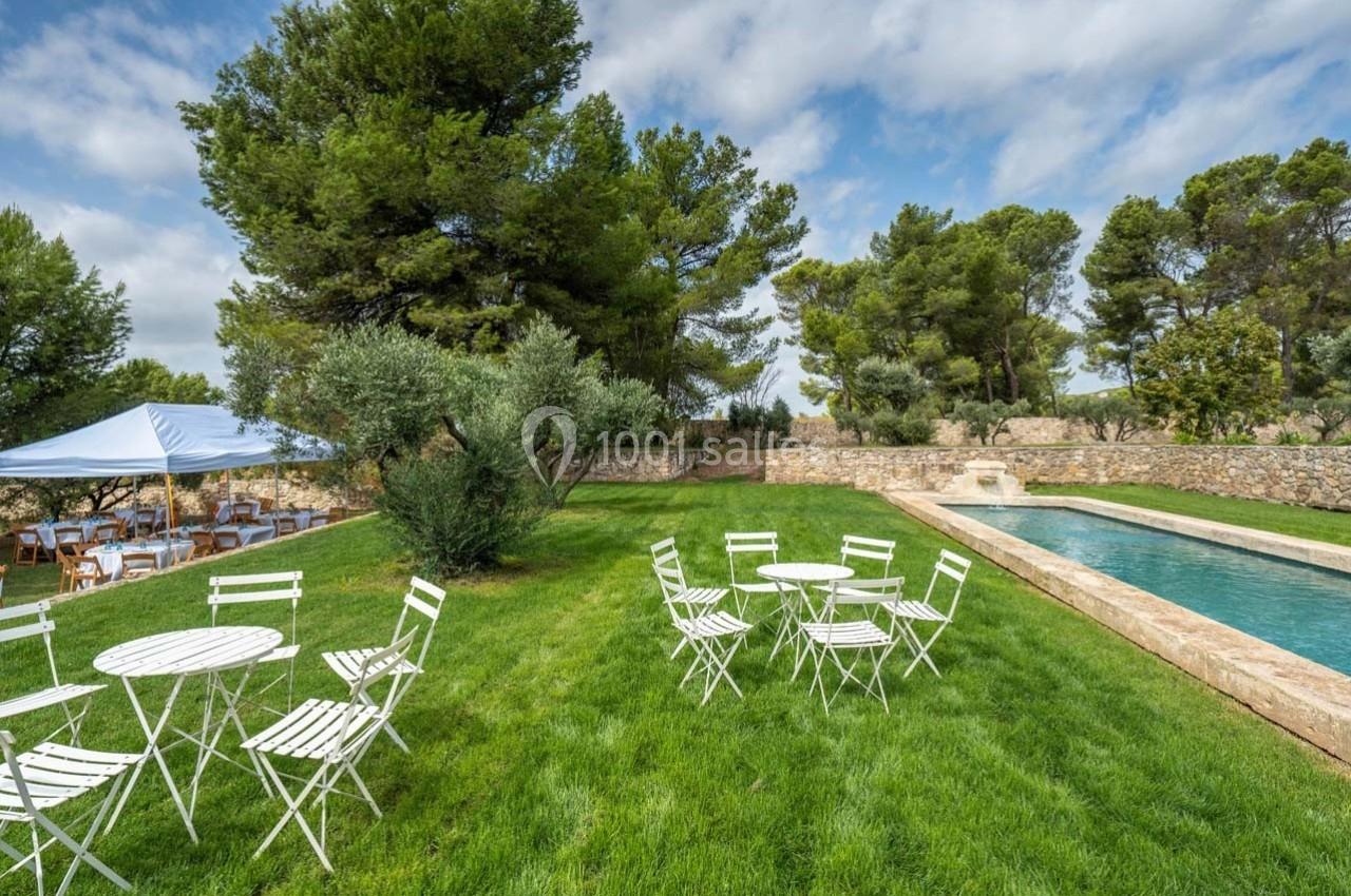 Jardin avec tables blanches, piscine rectangulaire, arbres et tente installée pour un événement en plein air.