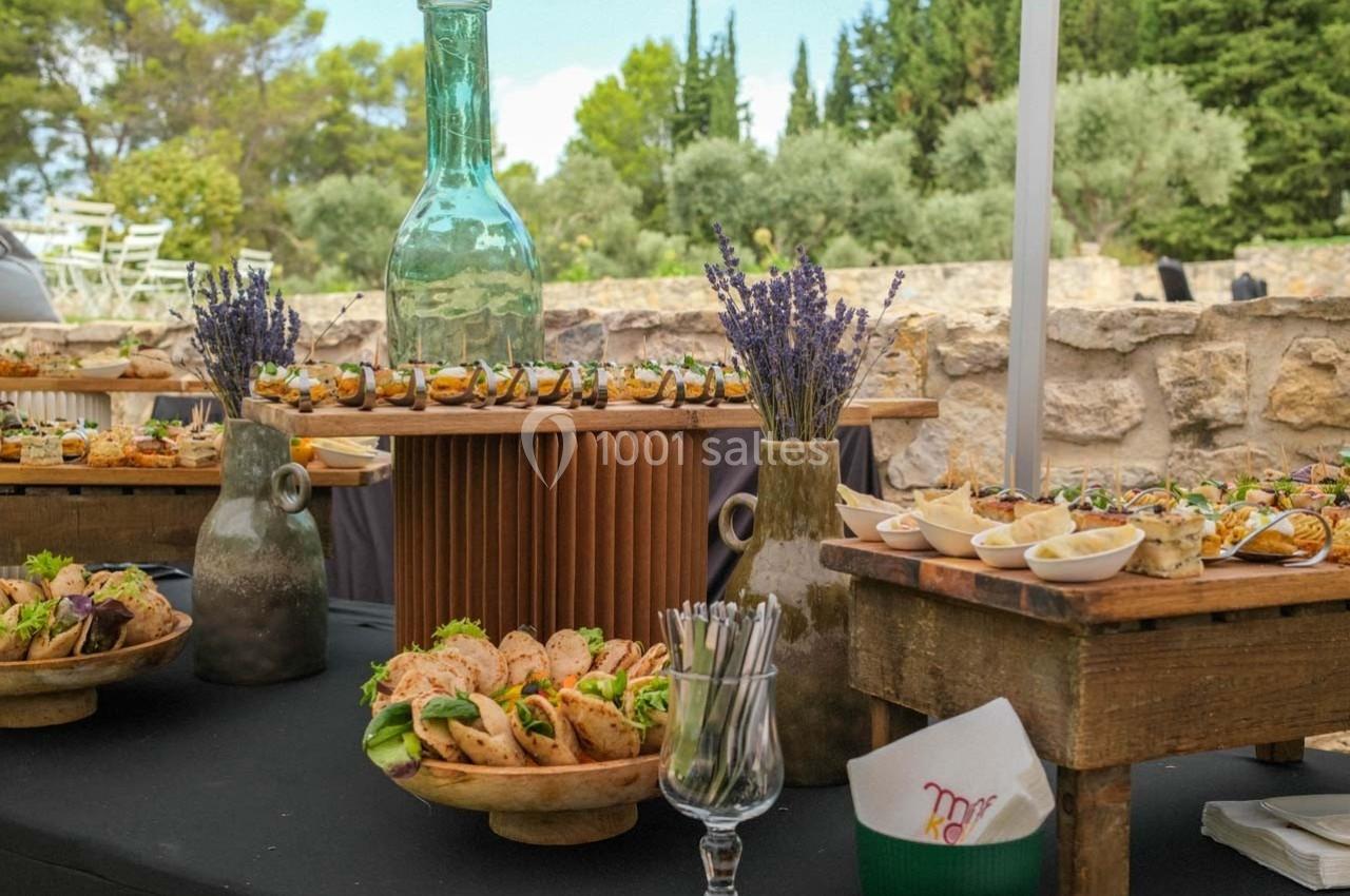 Buffet en plein air avec plats variés, décoré de lavande, bouteilles en verre et éléments rustiques.