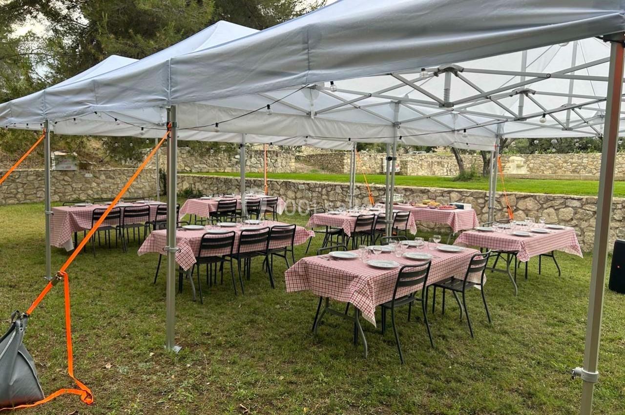 Tables dressées avec nappes à carreaux rouges sous des tonnelles blanches dans un espace extérieur herbeux.