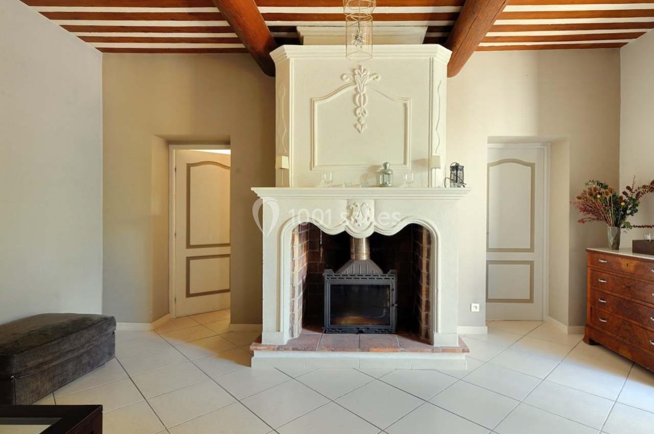 Cheminée en pierre blanche avec insert, entourée de murs clairs et poutres apparentes dans une pièce lumineuse.