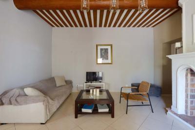 Salon avec canapé beige, fauteuils, table basse, télévision, cheminée en pierre et plafond avec poutres apparentes.