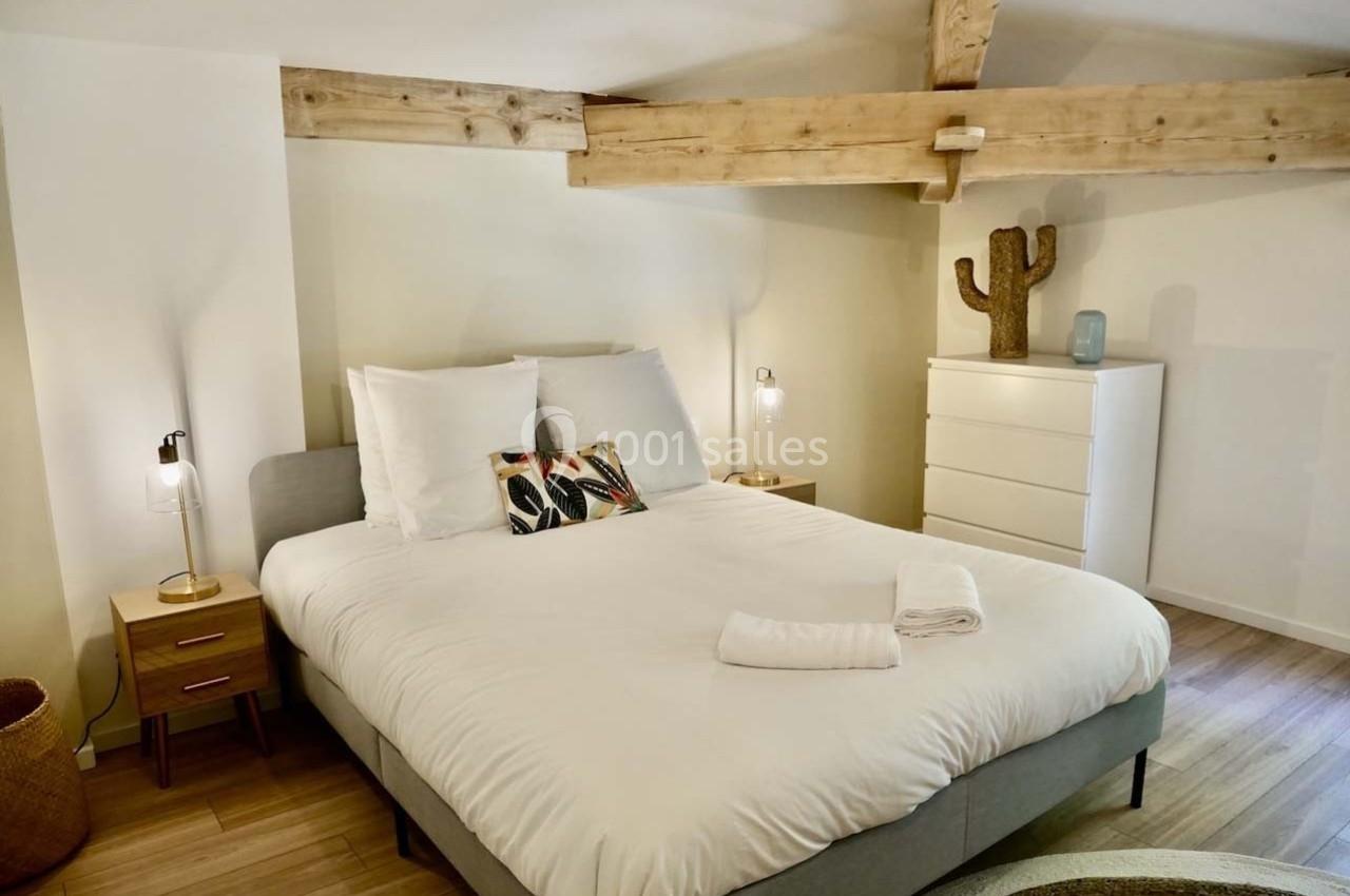 Chambre lumineuse avec lit double, poutres apparentes, tables de chevet, commode blanche et décoration en cactus.