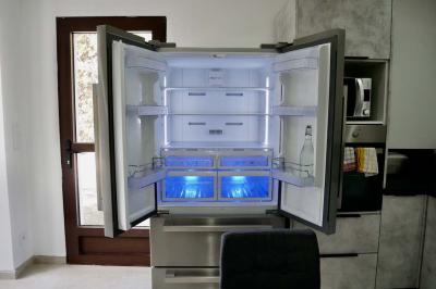 Salon avec canapé beige, fauteuils, table basse, télévision, cheminée en pierre et plafond avec poutres apparentes.