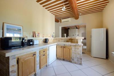 Salon avec canapé beige, fauteuils, table basse, télévision, cheminée en pierre et plafond avec poutres apparentes.