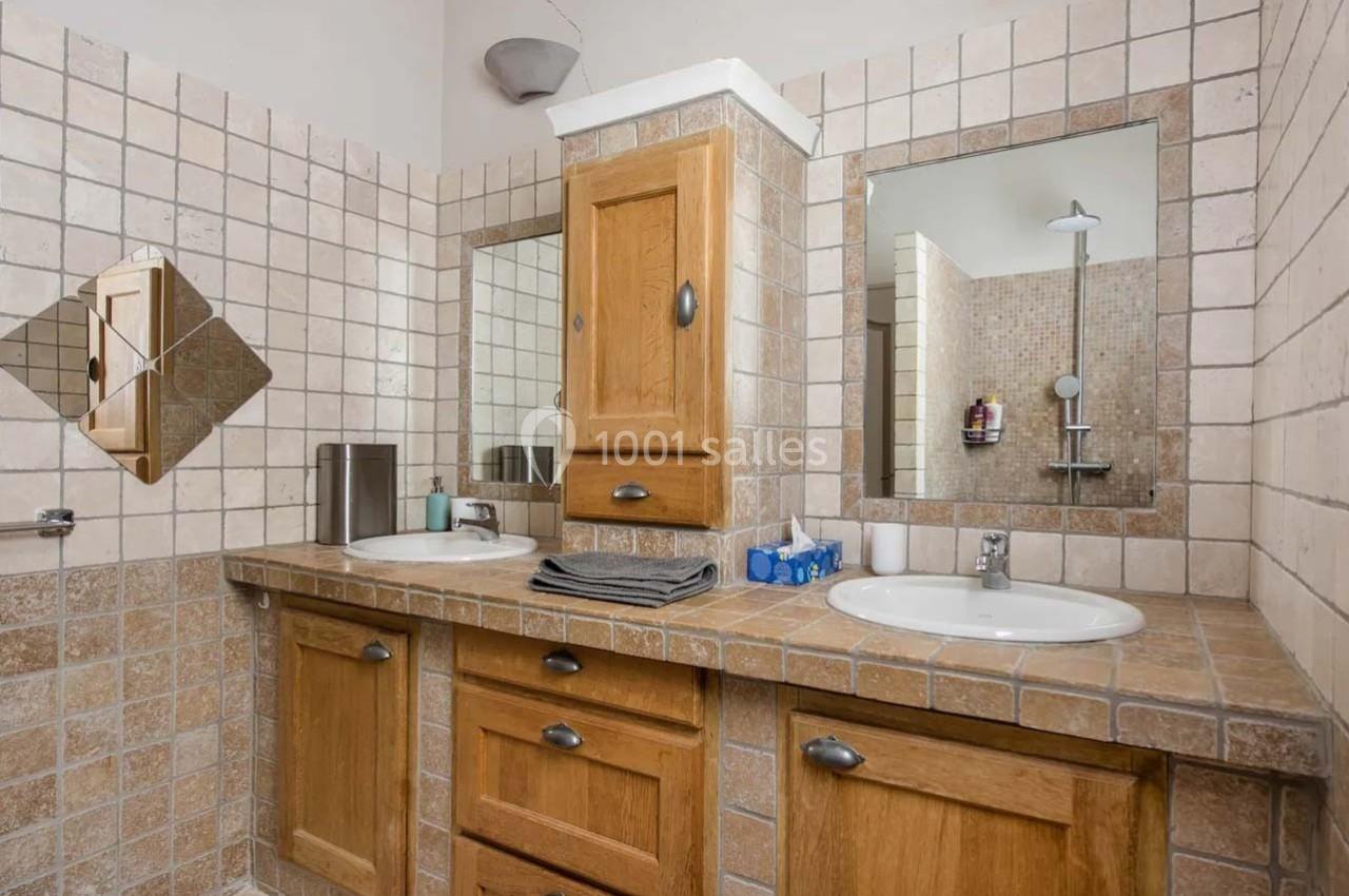 Salle de bain avec deux lavabos, meubles en bois, miroirs et carrelage beige sur les murs.